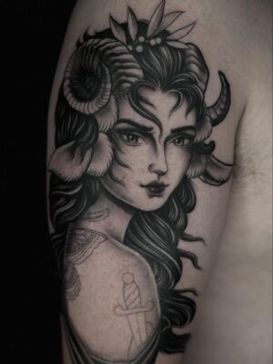 Upper arm tattoo of a mythical women with horns in black ink