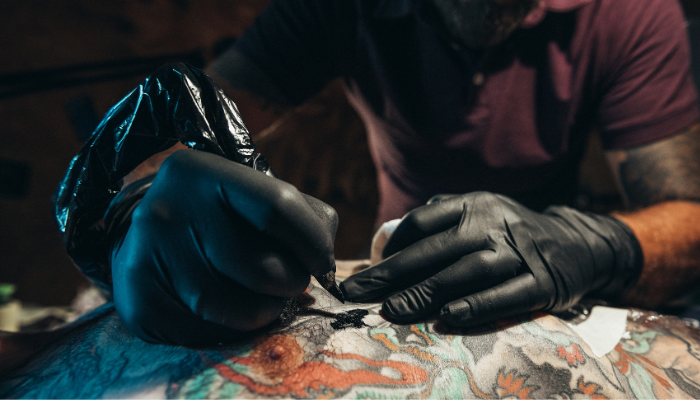 Close up of a tattoo artists wearing black gloves doing a tattoo