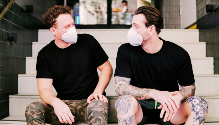 Two men wearing Covid masks, sitting on steps and looking at each other